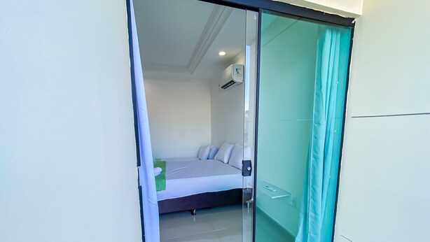 A modern bedroom with a glass door leading to a balcony, a bed with white linens, and a small bedside table. - Casa com 2 suítes praia de Taperapuã (Porto Seguro)