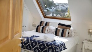 A bedroom with a skylight, a bed with striped pillows, a patterned blanket, and a nightstand with a lamp. - 4 Bed in Mumbles (oc-hh53) (The Mumbles)