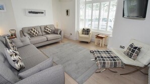 A modern living room with a grey sectional sofa, a small armchair, a white sofa, and a patterned throw. - 4 Bed in Mumbles (oc-hh53) (The Mumbles)