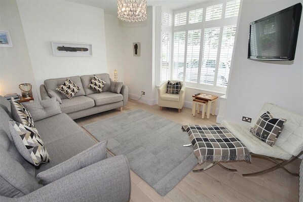 A modern living room with a grey sectional sofa, a small armchair, a white sofa, and a patterned throw. - 4 Bed in Mumbles (oc-hh53) (The Mumbles)