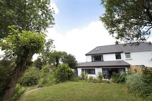 A two-story house with a white exterior and dark roof, surrounded by lush greenery and trees. - 2 Bed in Llanmadoc (oc-hh2110) (Llanmadoc)