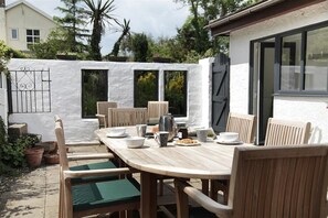 An outdoor patio with a wooden table and chairs, surrounded by a white wall with windows. - 2 Bed in Llanmadoc (oc-hh2110) (Llanmadoc)