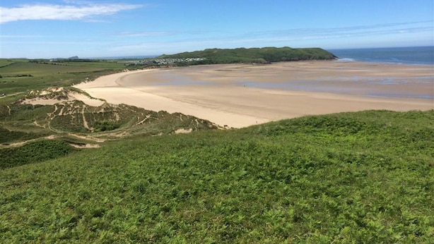 Un paysage côtier avec une plage de sable, des collines verdoyantes et un ciel dégagé.