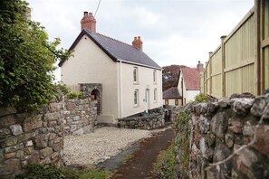 A narrow street with a white house featuring a stone wall on one side and a wooden fence on the other.