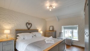 A bedroom with a large bed, bedside tables, a dresser, a chair, a window, and a ceiling light fixture. - 2 Bed in Llanmadoc (oc-hh469) (Llanmadoc)