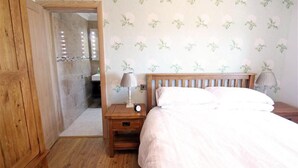 A bedroom with a wooden bed, nightstands with lamps, a wooden wardrobe, and a bathroom visible through an open door. - 1 Bed in Gower (oc-hh80) (Oxwich)