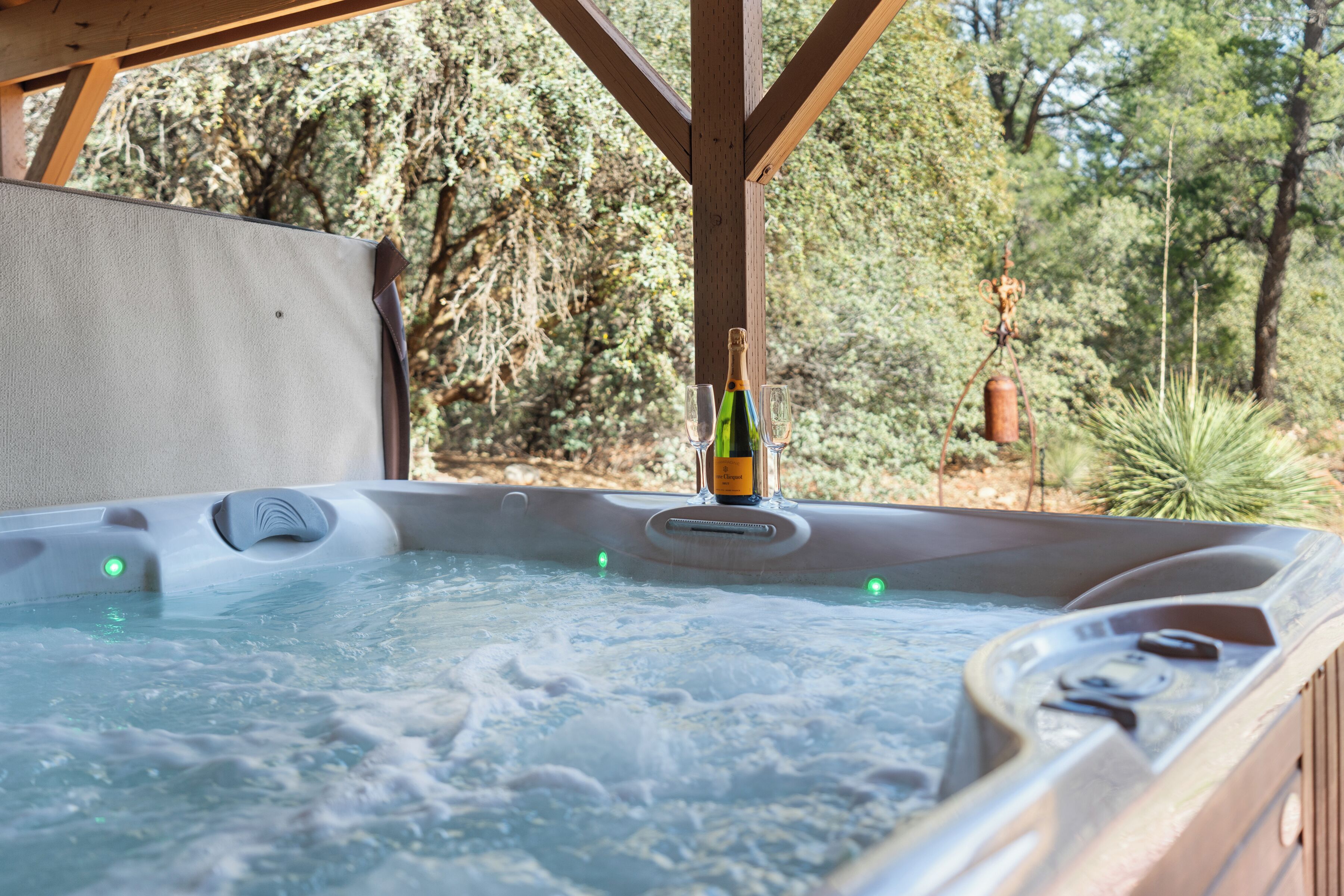 Un bain à remous avec une bouteille et des verres, entouré d’arbres.