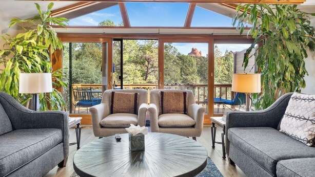 Un salon moderne avec deux canapés, une table basse et de grandes fenêtres donnant sur des arbres et une montagne.