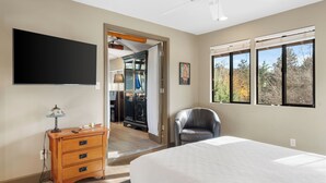 Une chambre à coucher avec un lit, un bureau avec une lampe, une chaise, un téléviseur et une fenêtre donnant sur des arbres.