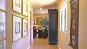 Un couloir orné de tableaux encadrés, un coin repas à l’arrière-plan et une grande porte en bois sombre.