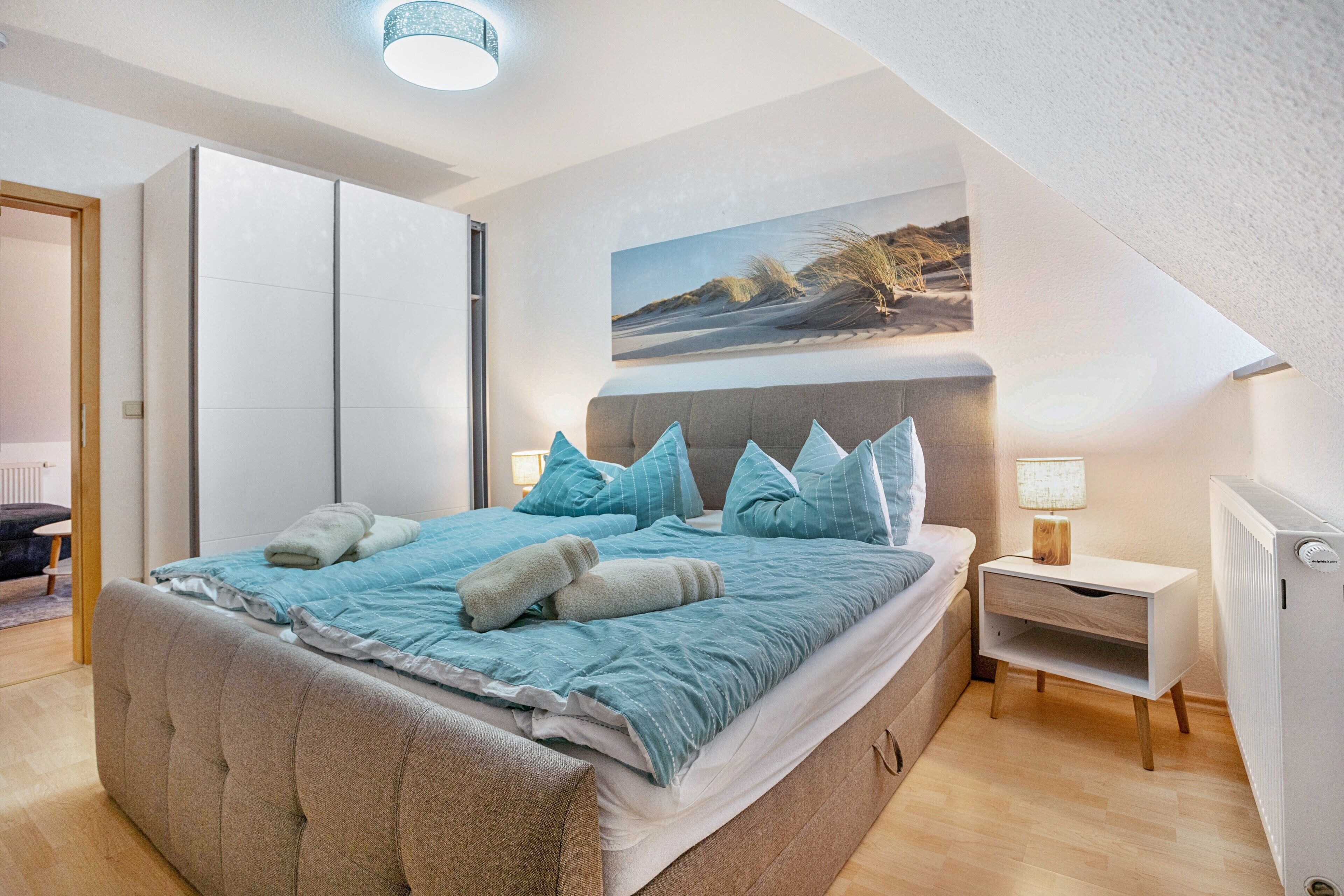 Una camera da letto con un letto, un comodino, una lampada e un quadro appeso al muro.