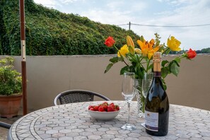 A round table with a bottle of wine, a bowl of strawberries, and a vase with flowers.