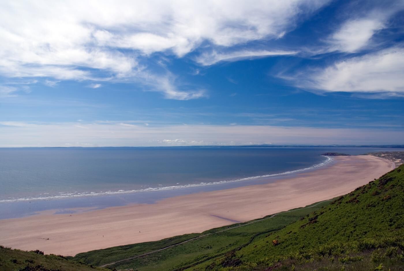 Eine Küstenlandschaft mit einem breiten Sandstrand und wolkenlosem Himmel.