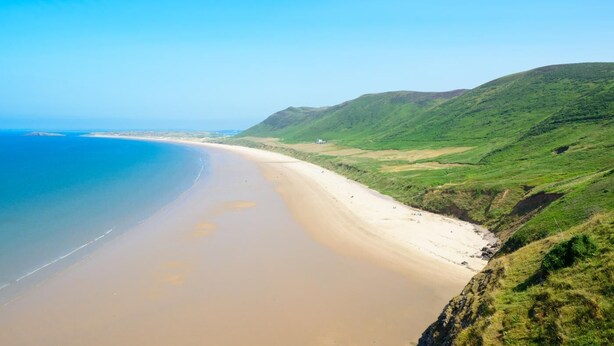 Eine Küstenlandschaft mit Sandstrand und grünen Hügeln.