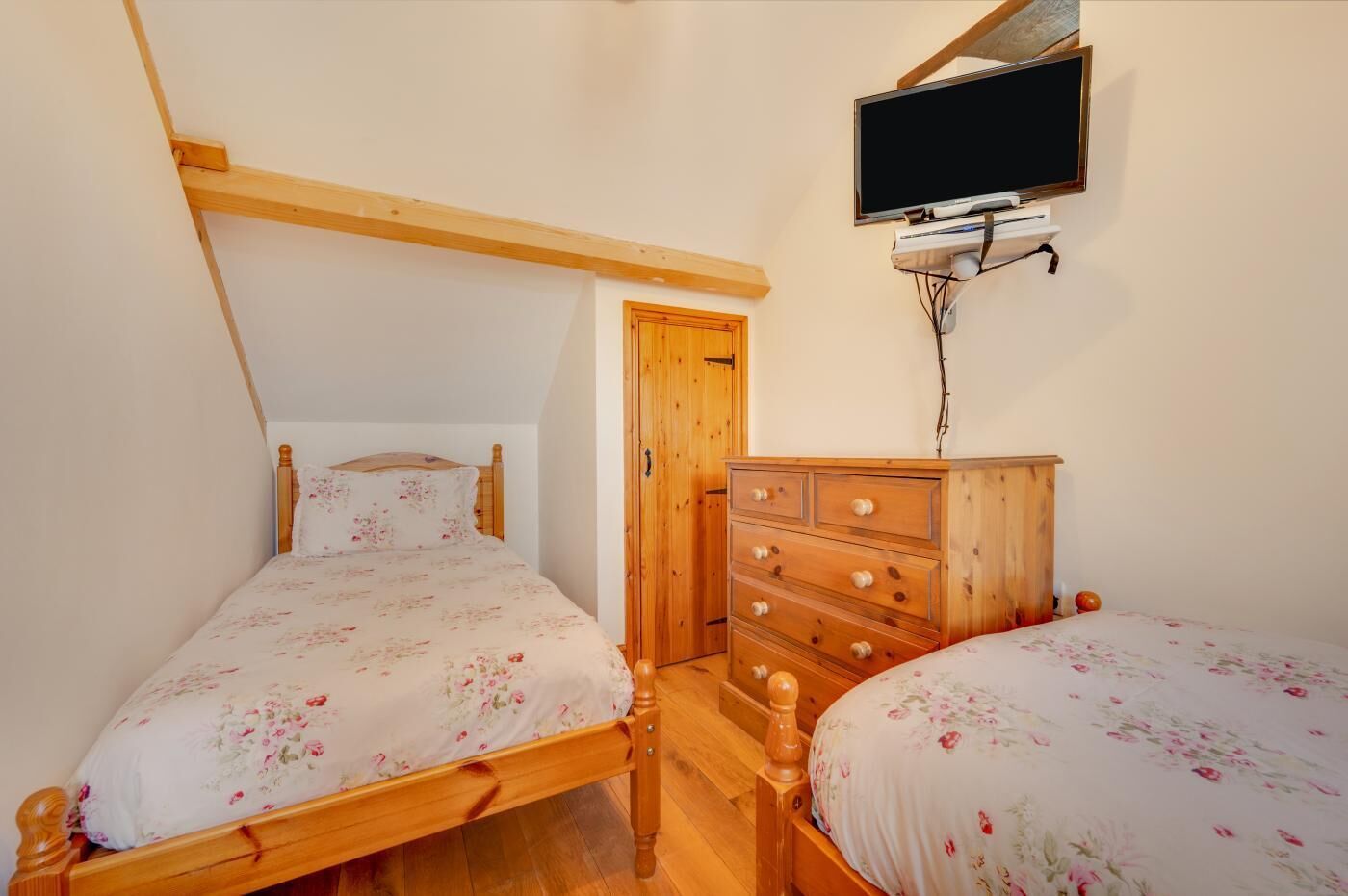 A bedroom with two wooden beds, a wooden dresser, a television mounted on the wall, and a wooden door.