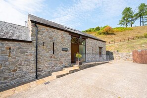 A stone building with a sloped roof, a wooden door, and a small porch with steps leading to the entrance. - 3 Bed in Gower (oc-hh407) (Cheriton)