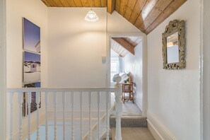 Een trap met een witte leuning die leidt naar een slaapkamer met een bed, nachtkastje en lamp.