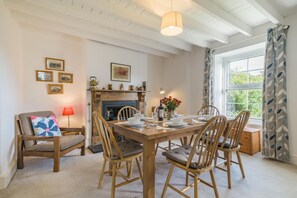 A dining area with a wooden table set for four, surrounded by wooden chairs, a fireplace, and framed pictures on the wall. - 3 Bed in Gower (oc-hh150) (Llangennith)