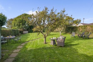 Een verzorgde tuin met gazon, een eettafel met stoelen, en een bijzettafeltje met kopjes en schotels.