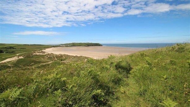 Een kustlandschap met een zandstrand, grasheuvels en een heldere lucht.