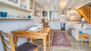 A cozy kitchen with a dining table set for two, wooden chairs, and a red patterned rug. - 1 Bed in Swansea (oc-hh404) (Llanmadoc)