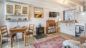 A cozy kitchen with a stove, a dining area with chairs, a bookshelf, and a TV mounted on the wall. - 1 Bed in Swansea (oc-hh404) (Llanmadoc)