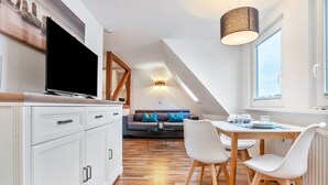 A modern kitchen with a TV, white cabinets, and a dining area with a table and chairs. - Apartment '4 Leuchtturm' with Shared Garden, Balcony and Wi-Fi (Seedorf)