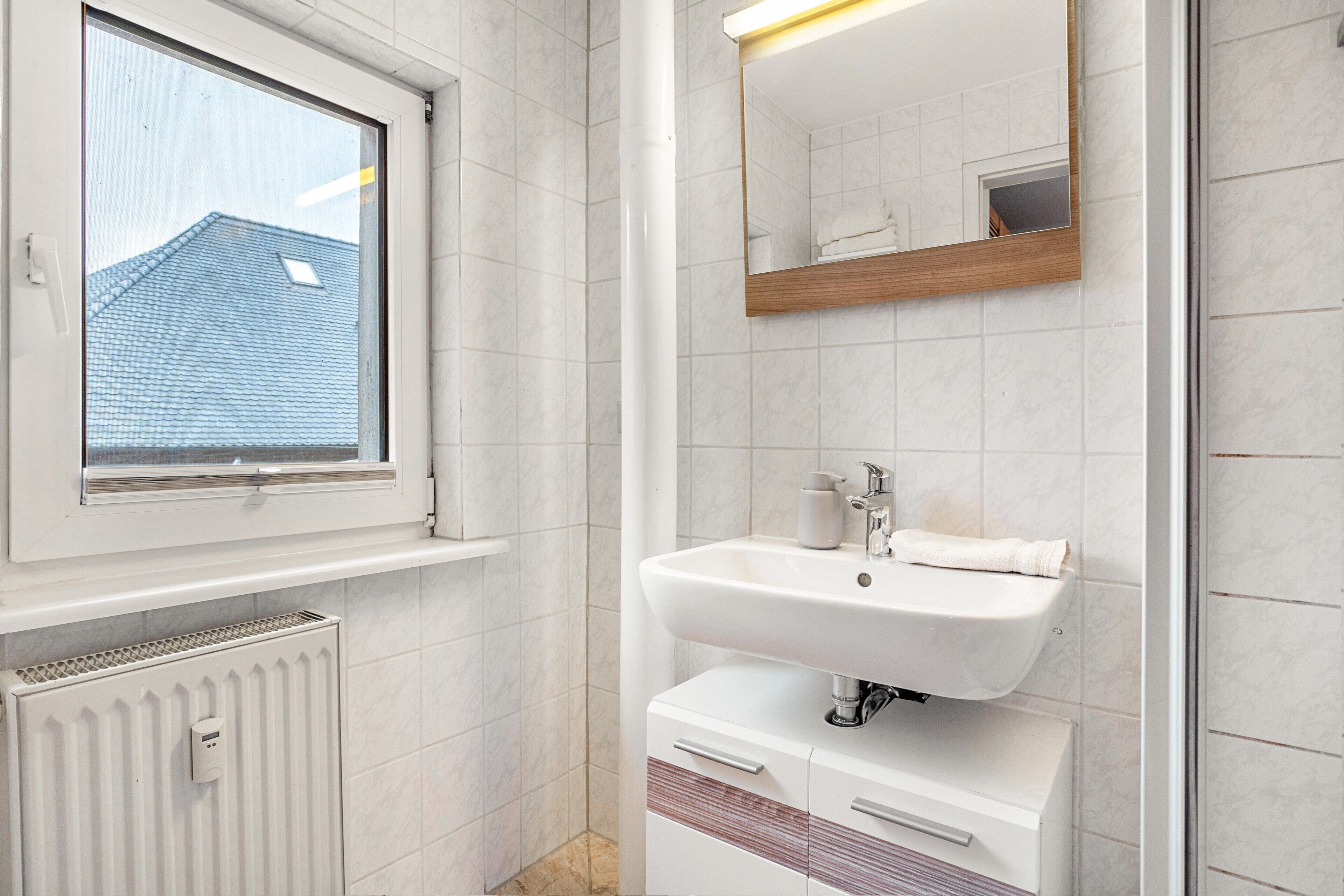 A bathroom with a window, a sink, a mirror, and a radiator.