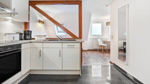 A modern kitchen with white cabinets, a black oven, and a wooden beam ceiling. - Apartment '4 Leuchtturm' with Shared Garden, Balcony and Wi-Fi (Seedorf)