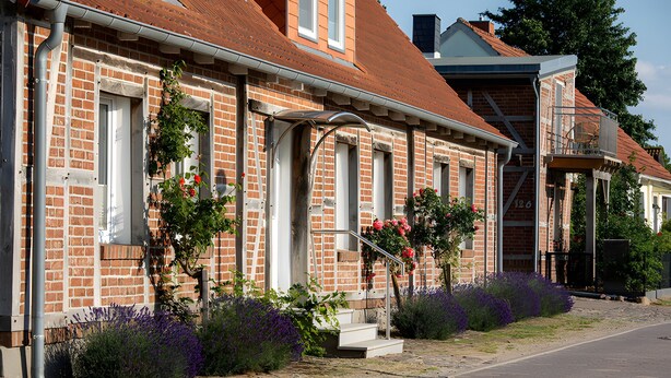 A brick building with a red-tiled roof, a staircase leading to a door, and a balcony with a metal railing. - Apartment '4 Leuchtturm' with Shared Garden, Balcony and Wi-Fi (Seedorf)