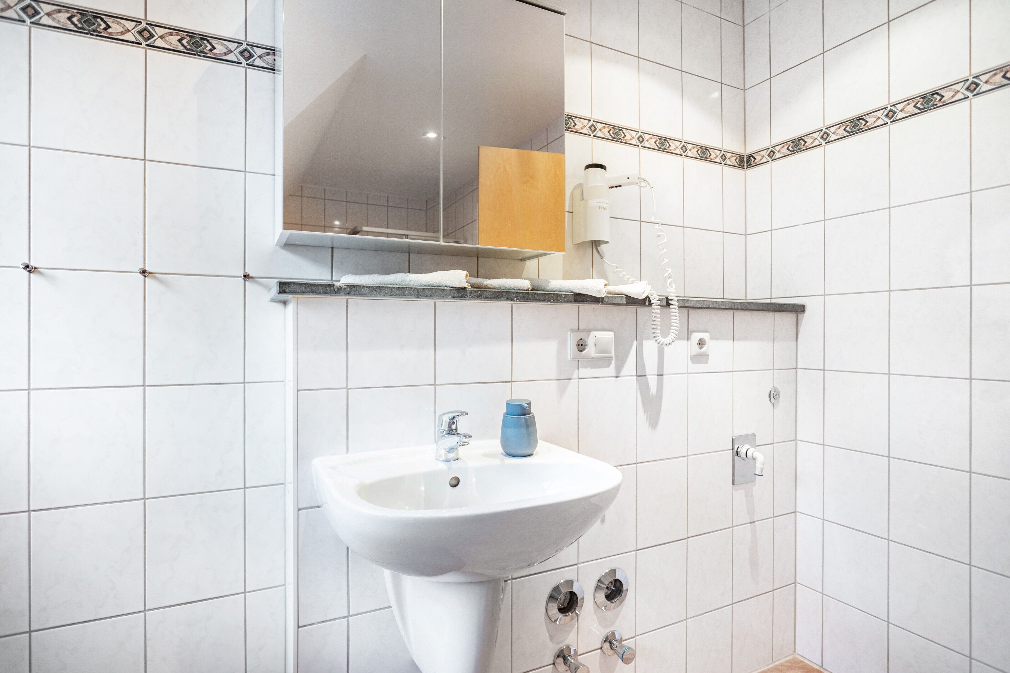 Een badkamer met een wit wastafel, een spiegel, een handdoekhouder en een douche.