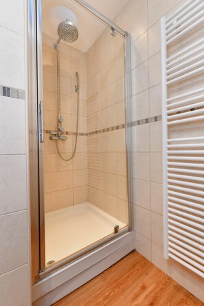 Een glazen douchecabine met een handdouche, een wandhanddoekhouder en een houten vloer.