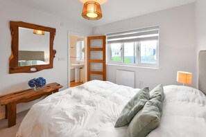 Een slaapkamer met een bed, een nachtkastje met een bloevas, een spiegel, een raam met uitzicht en een radiator.