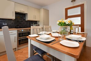Eine moderne Küche mit beigen Schränken, einer Holzarbeitsplatte und einer Essecke für vier Personen.