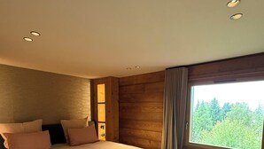 Un dormitorio moderno con una cama grande, un banco, paredes de madera y una ventana con vistas a un bosque.