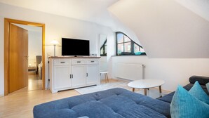 A modern living room with a sofa, a television, a cabinet, and a window. - Apartment 'Ferienwohnung 5 Seebrücke' with Lake View, Private Terrace and Wi-Fi (Sellin)