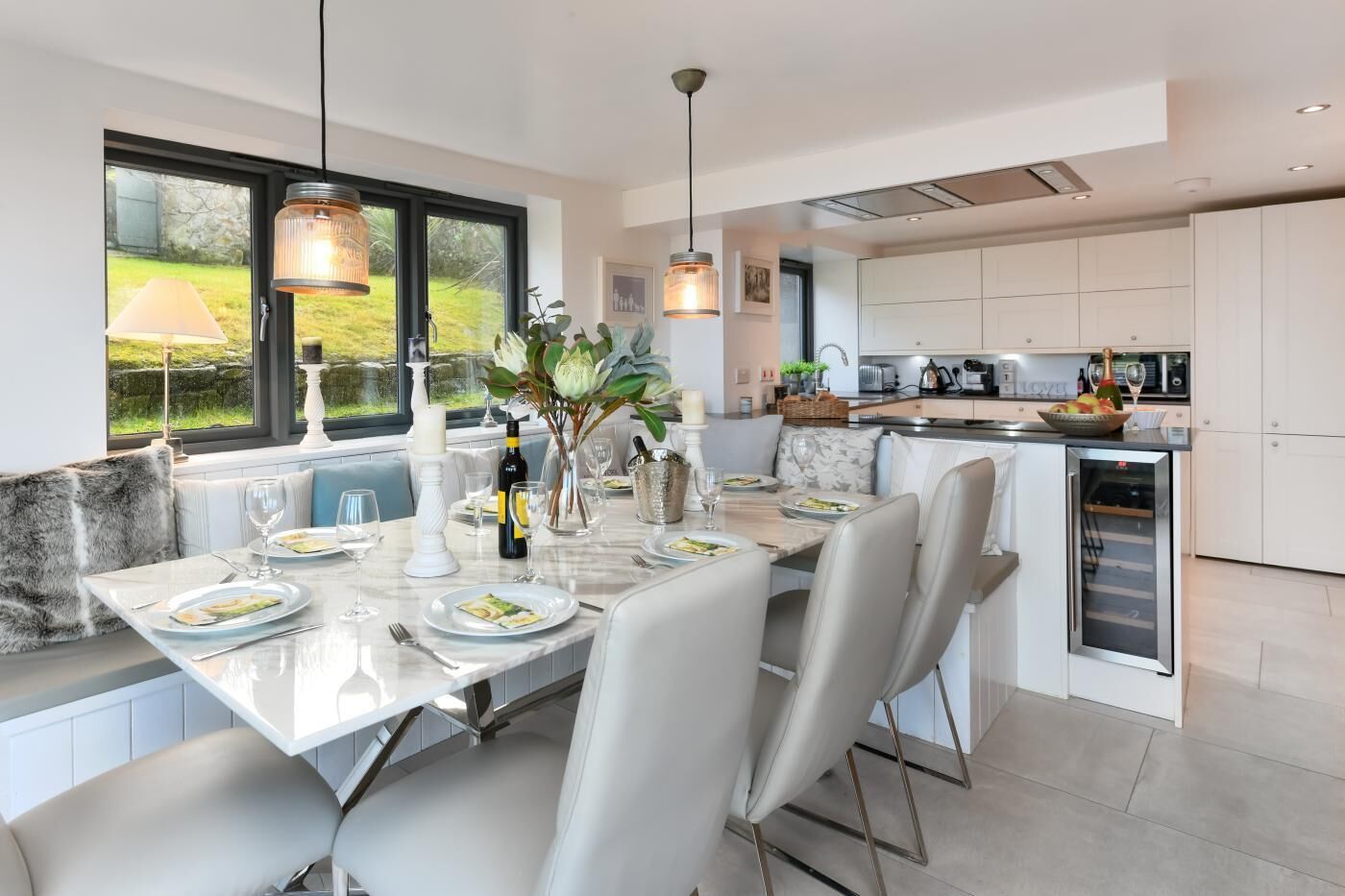 A modern kitchen with white cabinetry, a dining area with a marble table, and a view of the outdoors through large windows.