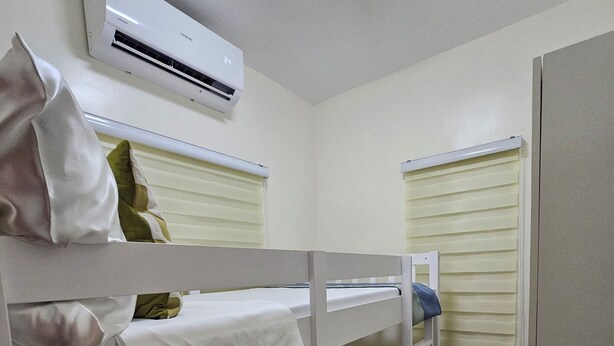 Une chambre avec un lit superposé, un climatiseur fixé au plafond, une fenêtre avec des stores et une porte.