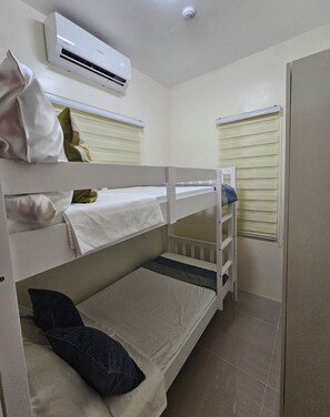 Habitación con literas, aire acondicionado en el techo, ventana con persianas y una puerta.