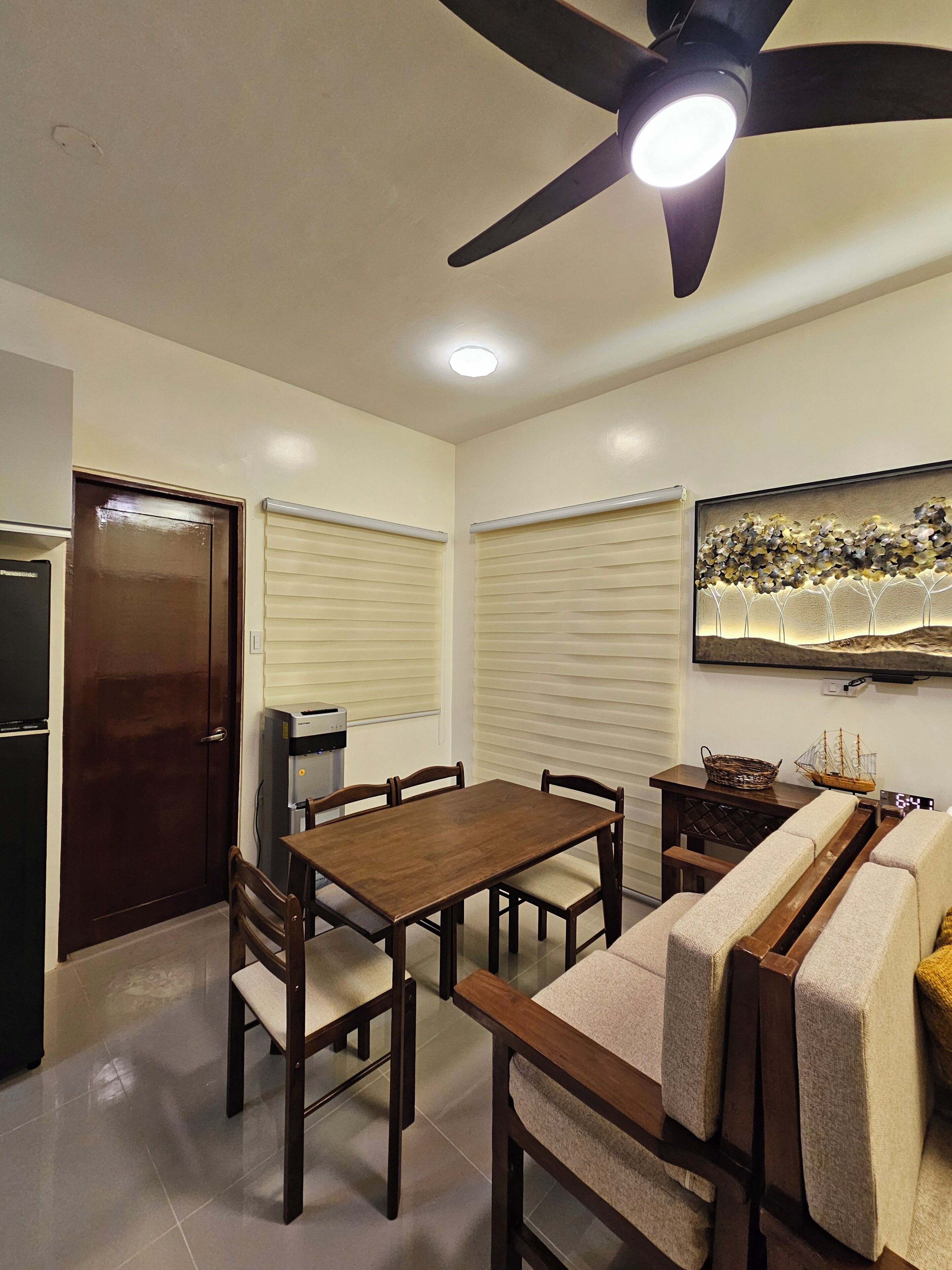 A dining area with a table and chairs, a ceiling fan, a water dispenser, and a wall-mounted TV.