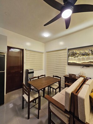 A dining area with a table and chairs, a ceiling fan, a water dispenser, and a wall-mounted TV. - Cozy 3-bedroom house in charming Dauis, Panglao Island, Bohol (Dauis)