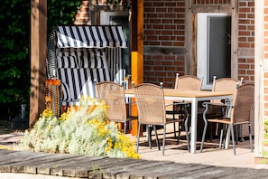 Une terrasse extérieure avec une table en bois et des chaises en osier, un auvent à rayures et un mur en briques.