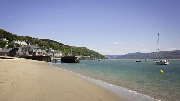 A beach with a pier, boats, and buildings on a hillside. - 2 Bed in Machynlleth (oc-bow39) (Darowen)