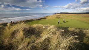 A coastal golf course with a clear view of the ocean, grassy dunes, and a few golfers on the green. - 2 Bed in Machynlleth (oc-bow39) (Darowen)