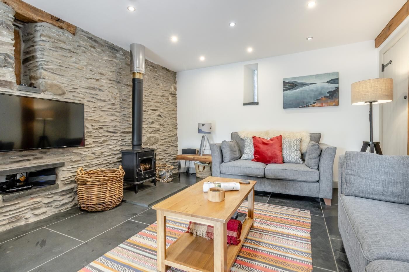 Una sala de estar moderna con una pared de piedra, una chimenea, un sofá gris, una mesa de centro de madera y un televisor de pantalla plana.