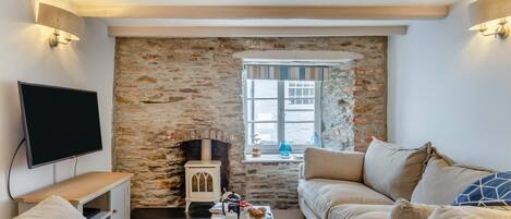 Un salon chaleureux avec un mur en pierre, une cheminée, un téléviseur et un canapé confortable.