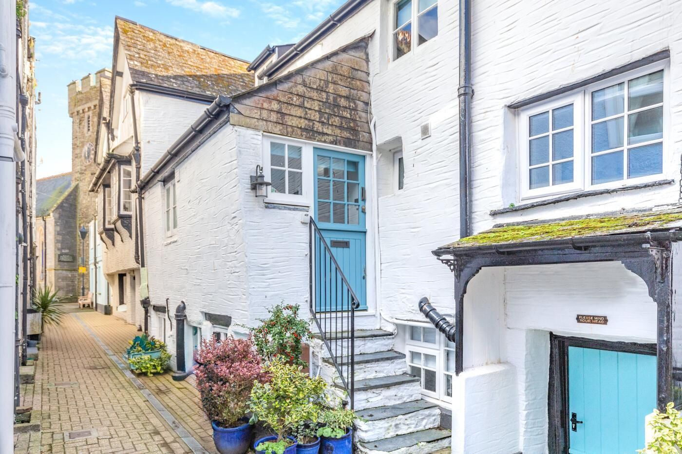 A narrow street with white buildings, a blue door, and potted plants.
