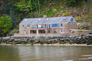 Un bâtiment en pierre doté de nombreuses fenêtres et d’un toit en pente, situé au bord d’une côte rocheuse.