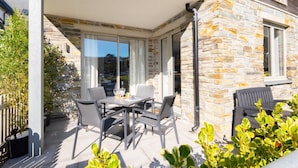 En overdækket terrasse med bord og stole, stenvægge og en glasdør, der fører ind i huset.