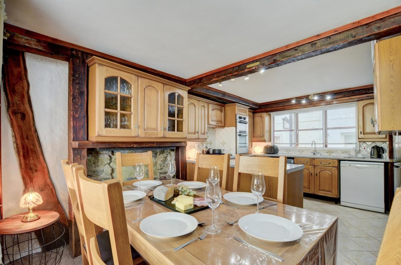 A dining area with a table set for four, wooden cabinets, a stone wall, and a small round table with a lamp.